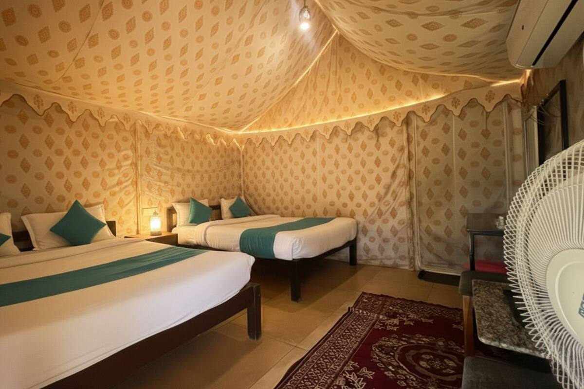 A room with two beds, a patterned wall, a red carpet, and a white fan.