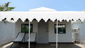 Ein modernes Gebäude mit weißer Fassade, einer überdachten Terrasse mit zwei Liegestühlen und einer großen, zeltartigen weißen Struktur auf dem Dach.
