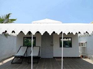 A modern building with a white exterior, a covered patio area with two lounge chairs, and a large white tent-like structure on the roof.