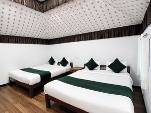A hotel room with two single beds, each with a green accent pillow, a wooden nightstand, and a patterned ceiling.