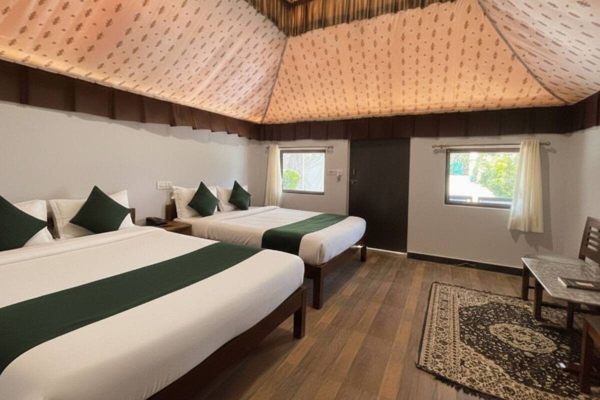 A hotel room with two beds, a wooden floor, a small table, and a window with curtains.