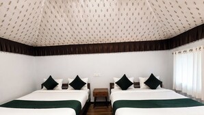 A hotel room with two beds, each with a green bedspread and white bedding, a wooden floor, and a patterned ceiling.