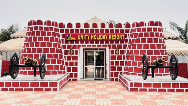 A building with a red brick facade, a sign reading 'UNITY HOLIDAY RESORT,' and two cannons on either side of the entrance.