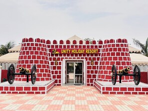 A building with a red brick facade, a sign reading 'UNITY HOLIDAY RESORT,' and two cannons on either side of the entrance.