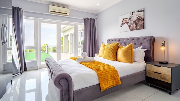 Quarto moderno com cama grande, mesa de cabeceira e vista para uma varanda.
