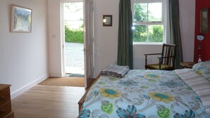 A bedroom with a bed, a chair, a door leading outside, and a window with curtains. - Swallow cottage (Kilgetty)