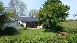 A house with a large lawn, a patio with chairs, and a tree in the foreground. - Swallow cottage (Kilgetty)