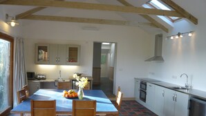 A kitchen with wooden beams, a dining table with chairs, a vase with flowers, and a sink. - Swallow cottage (Kilgetty)