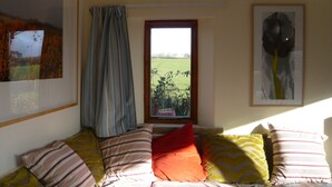 A room with a bed, a window with a view of a field, and two framed artworks on the wall. - Swallow cottage (Kilgetty)
