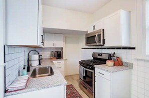 Une cuisine de taille réduite, avec des meubles blancs, un évier en acier inoxydable, un four à micro-ondes et une cuisinière.