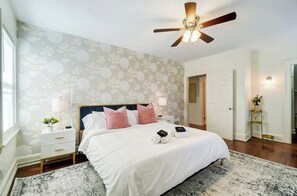 Une chambre à coucher avec un lit, une table de chevet, une lampe, un ventilateur de plafond et un papier peint à motifs floraux.
