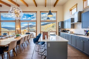 A modern kitchen with a large island, wooden beams, and large windows offering a view of the mountains. - Modern Mountain Retreat | Resort Amenities | Spacious layout (Silverthorne)