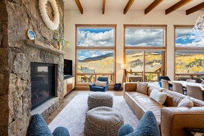A spacious living room with a stone fireplace, large windows with mountain views, and comfortable seating. - Modern Mountain Retreat | Resort Amenities | Spacious layout (Silverthorne)