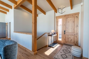 Una escalera de madera que lleva a una puerta, una silla azul y un tapete estampado.