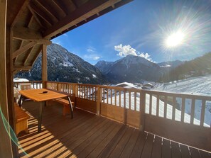 A wooden deck with a table and chairs, overlooking a snowy mountain landscape.