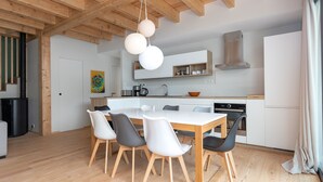 Una cucina moderna con soffitto in legno, mobili bianchi e zona pranzo con tavolo e sedie bianche.
