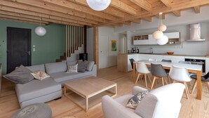 Un soggiorno moderno con divano, tavolino e zona pranzo con sedie. Si nota una cucina con pensili bianchi e un fornello.