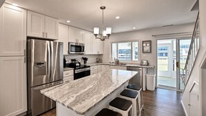 A modern kitchen with stainless steel appliances, a marble island, and a view to the outside.