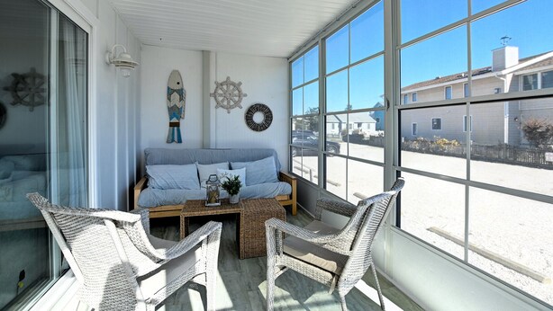 A sunlit room with a bed, wicker chairs, and a view of the street.