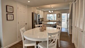 A modern kitchen with white cabinetry, a central island, and a dining area with a white table and chairs.
