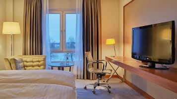 Une chambre d’hôtel comprenant un lit, un bureau avec une télévision, une chaise, une table avec des verres et des rideaux.