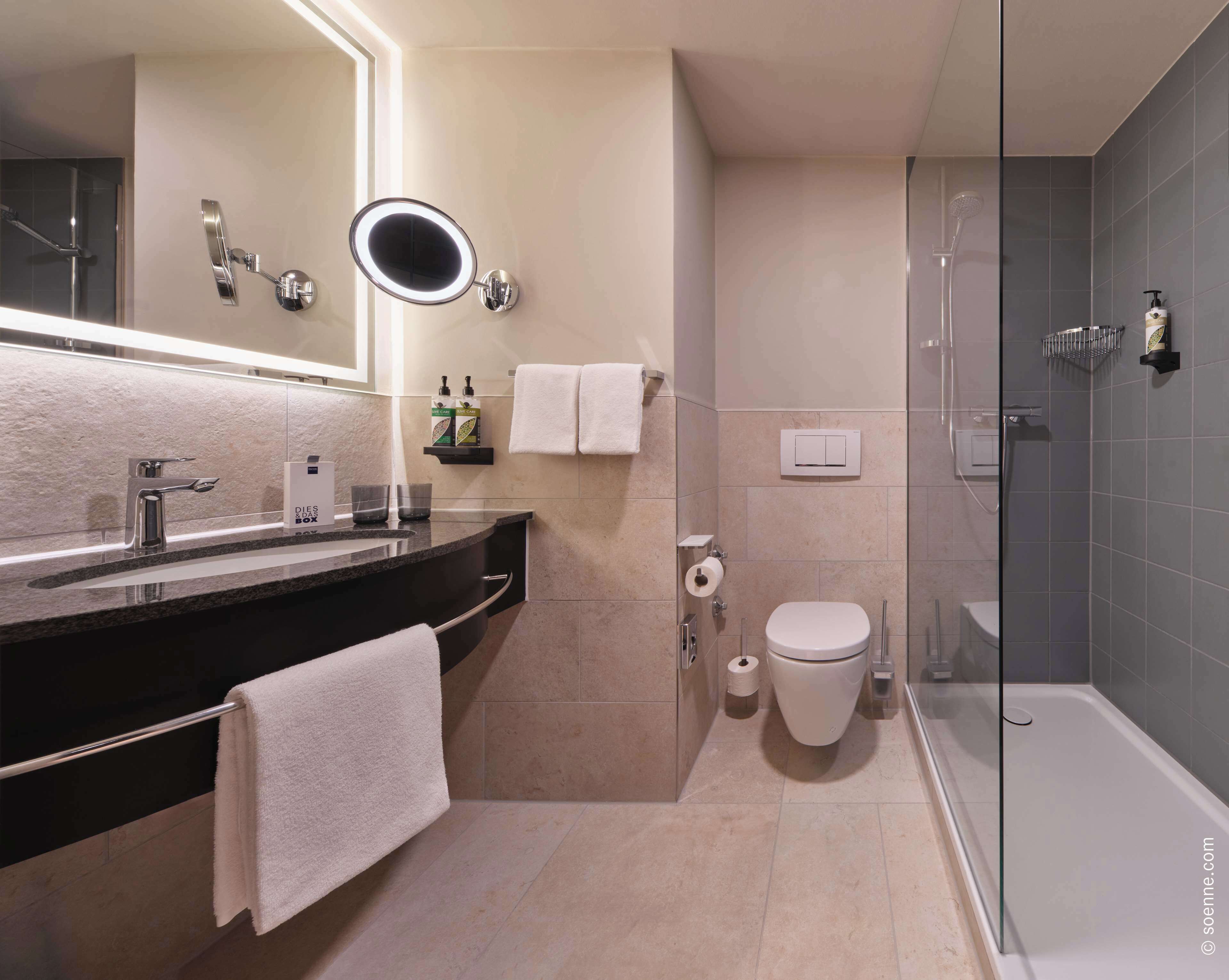Ein modernes Badezimmer mit einer gläsernen Duschkabine, einem Waschbecken mit Spiegel und einer Toilette.
