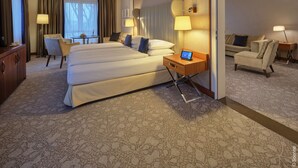 A hotel room with a large bed, two bedside tables, a desk, a chair, and a sofa. - Dorint Hotel Bonn (Bonn)