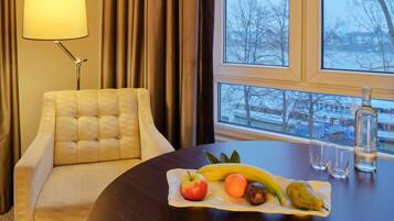 Habitación de hotel con una mesa redonda, un sillón con reposabrazos, una lámpara y un ventanal con vistas a árboles y edificios.