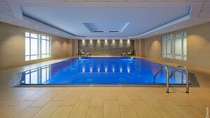 A large indoor swimming pool with clear blue water, surrounded by beige tiled walls and a stone accent wall. - Dorint Hotel Bonn (Bonn)