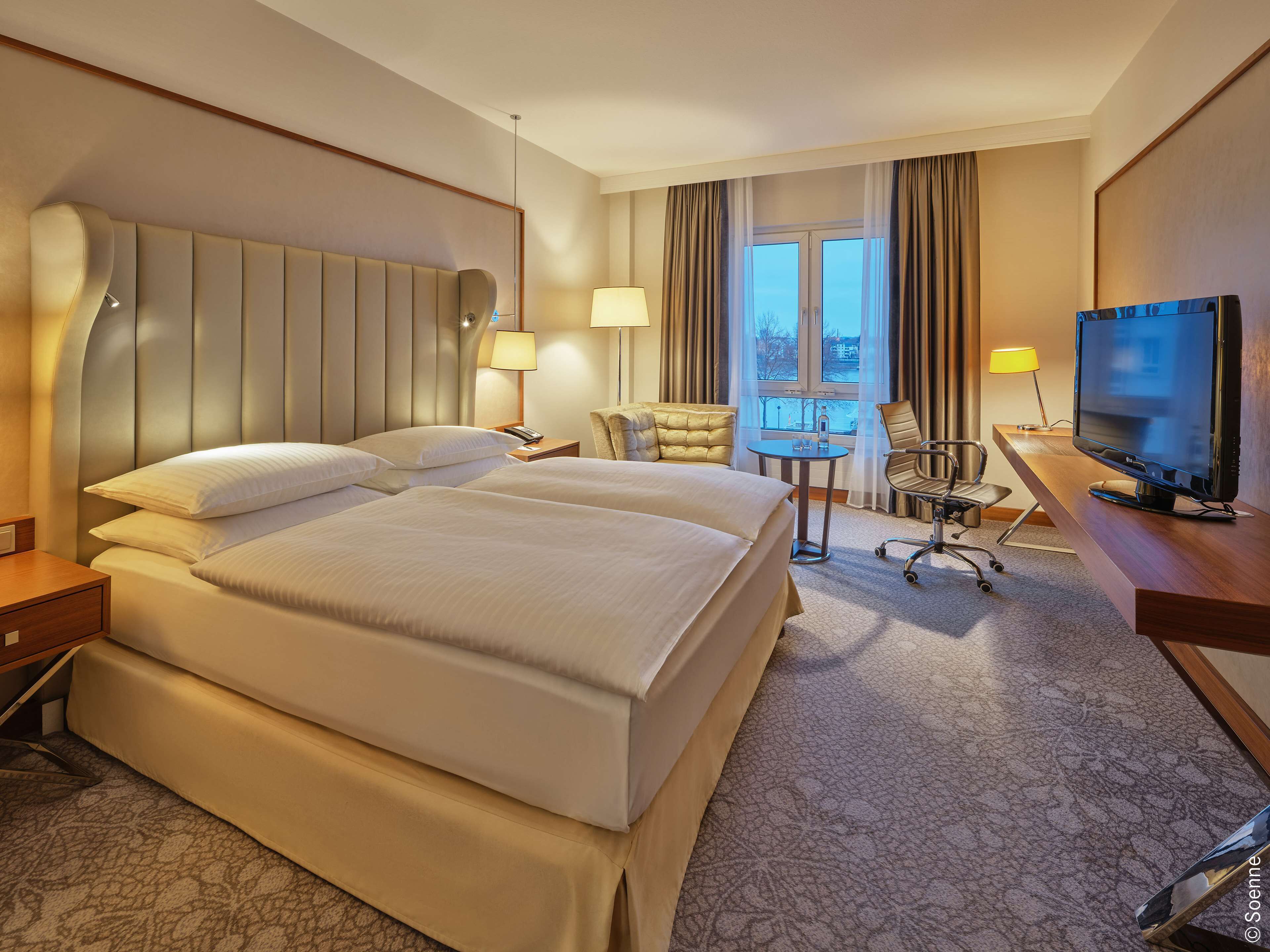Une chambre d’hôtel avec deux lits, un bureau, une télévision et une vue sur la ville par la fenêtre.