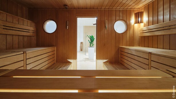 A sauna with wooden benches and a central aisle, leading to a glass door. - Dorint Hotel Bonn (Bonn)