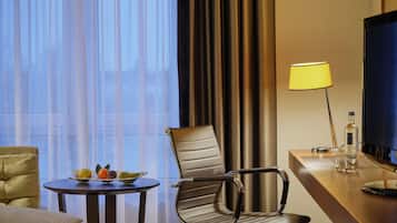 A hotel room with a bed, a dining table with fruit, a chair, a TV, and a lamp.