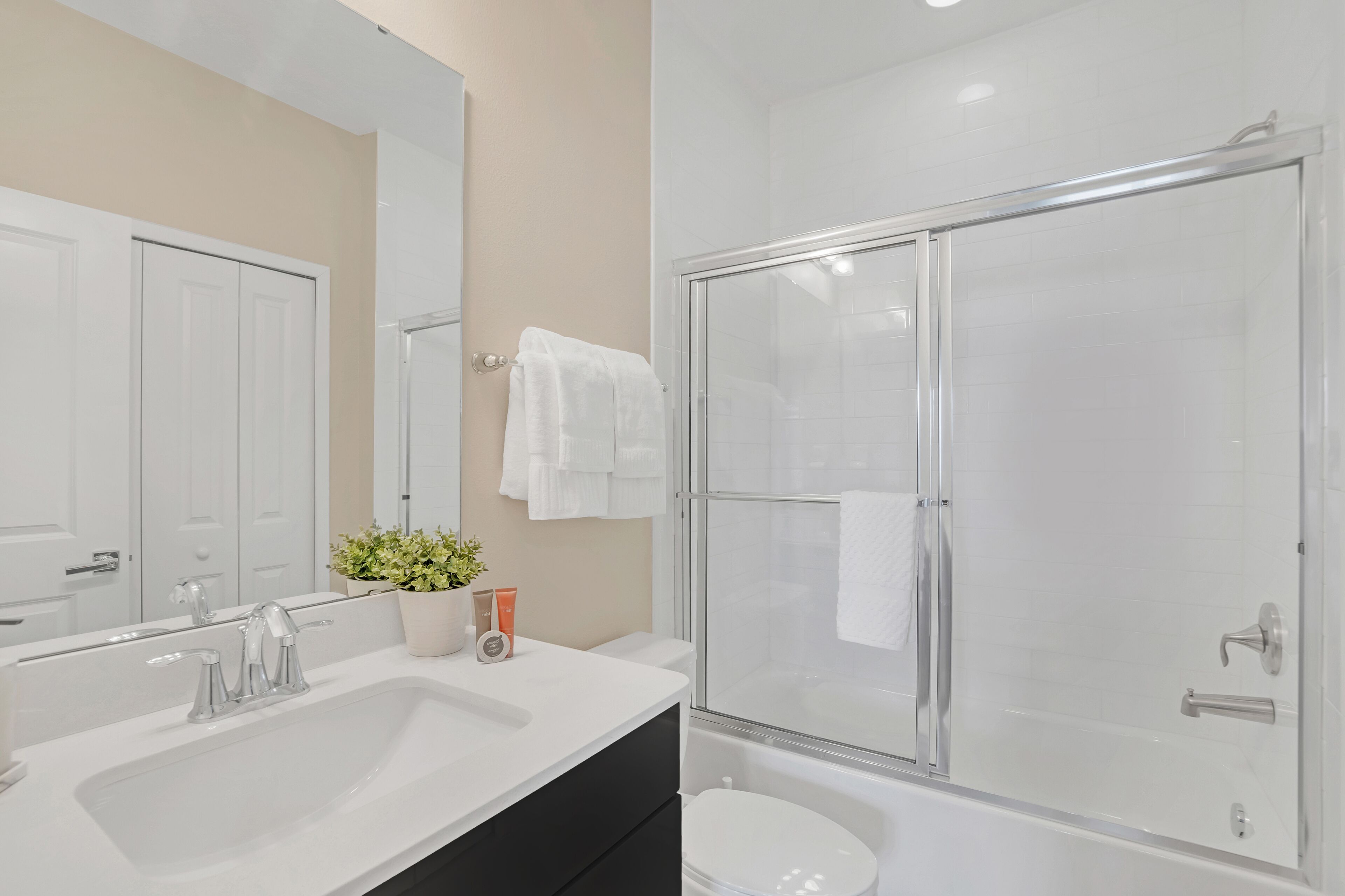 A modern bathroom with a double sink, a glass-enclosed shower, and a potted plant on the counter.