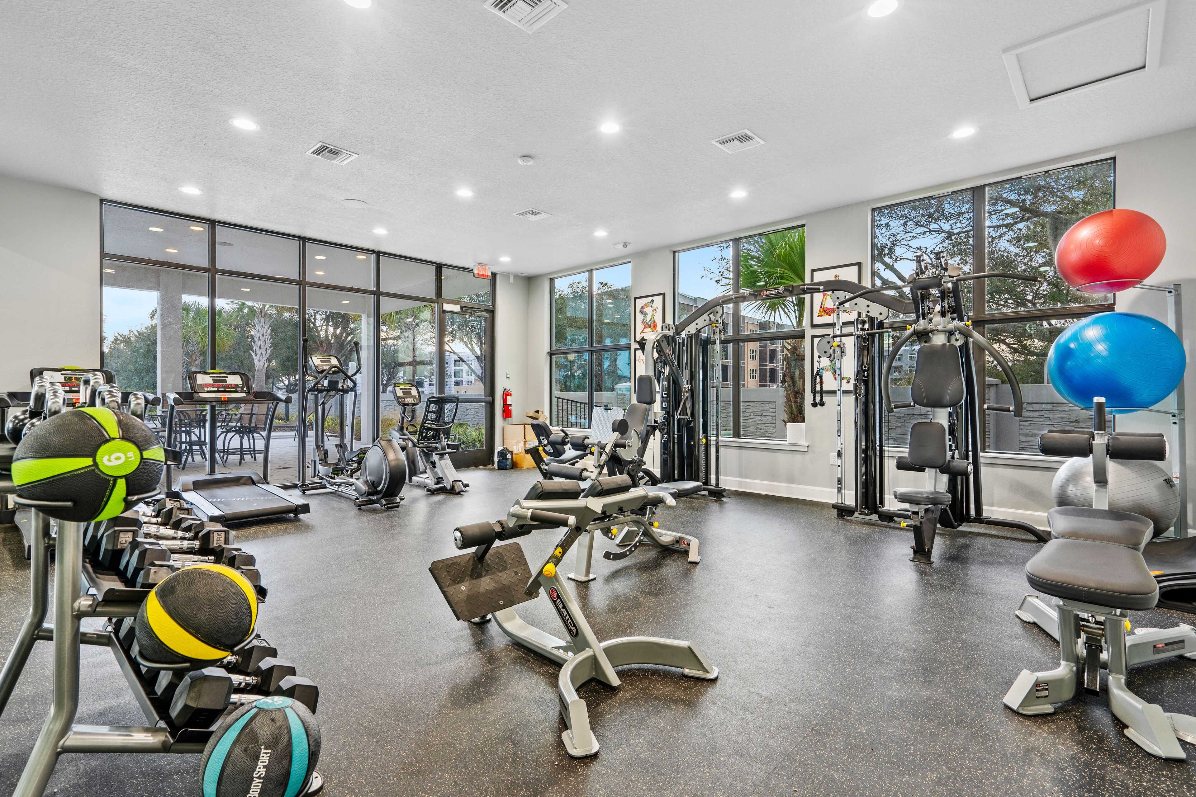 A gym with various exercise equipment, large windows, and a view of the outdoors.