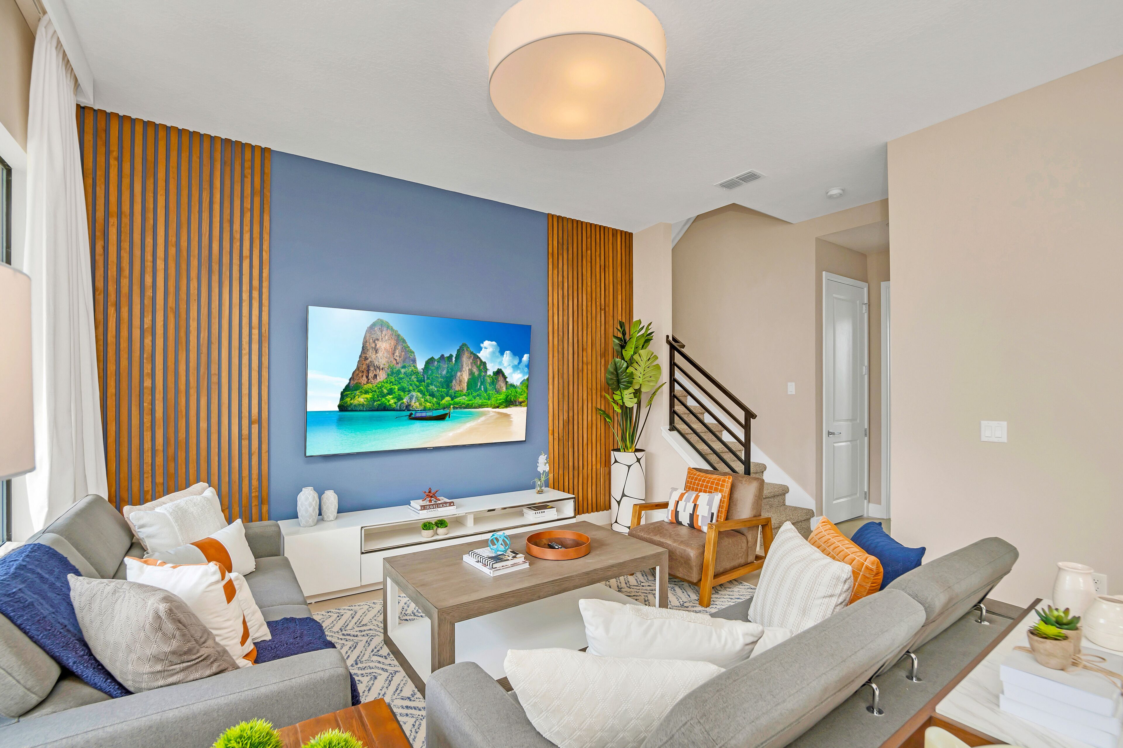 A modern living room with a large flat-screen TV, a sofa, a coffee table, and a staircase leading to another level.