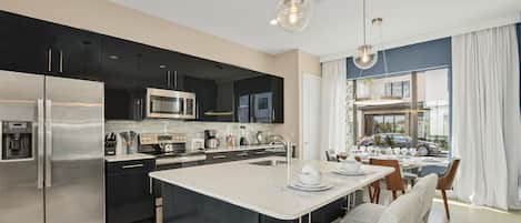 A modern kitchen with a central island, stainless steel appliances, and a dining area with a view.