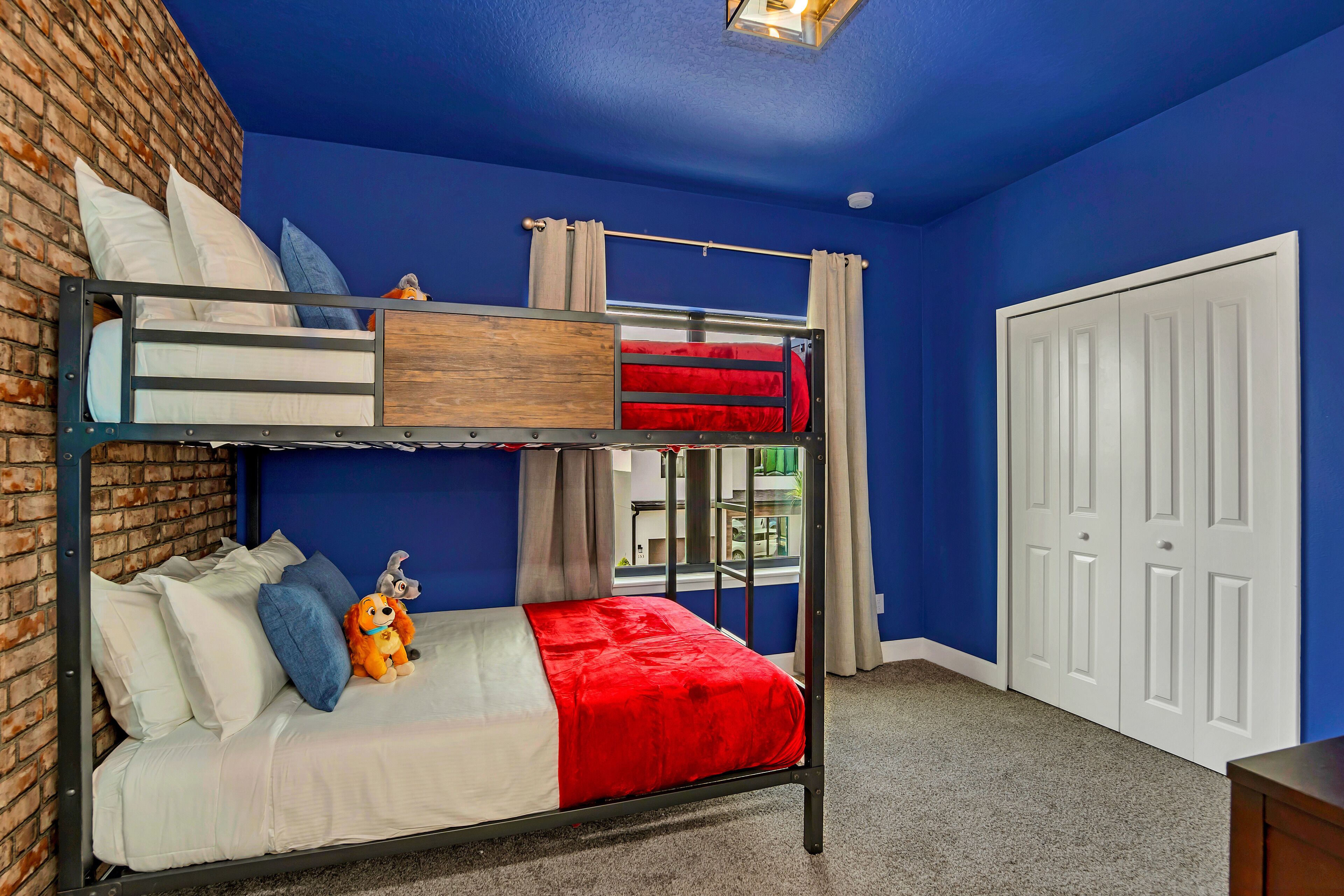 A bunk bed with a lower bunk and a single bed, both with white bedding and red accents. A plush toy is on the lower bunk.