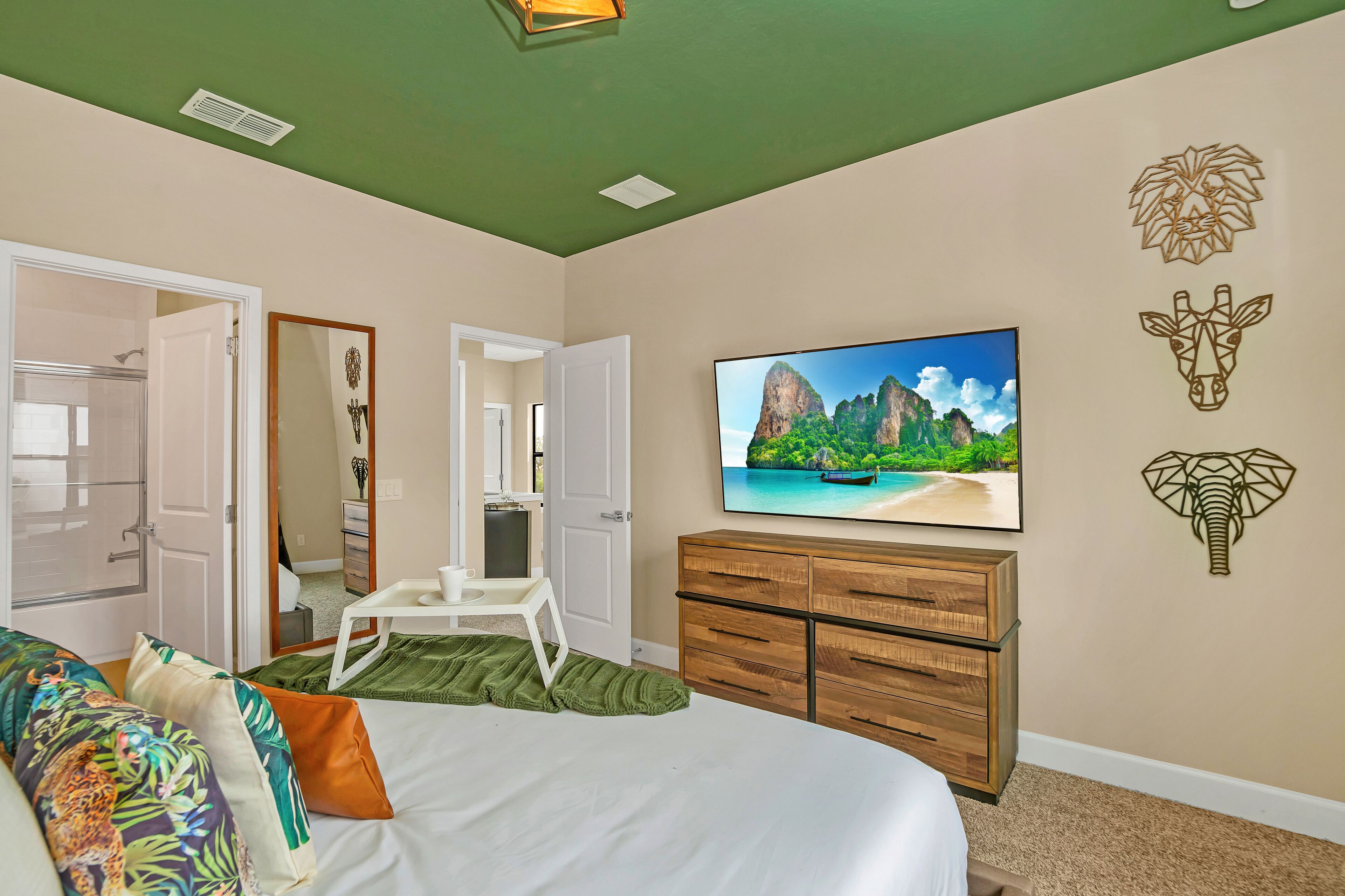 Une chambre à coucher avec un lit, une télévision, une commode en bois et un tableau représentant une scène de plage.