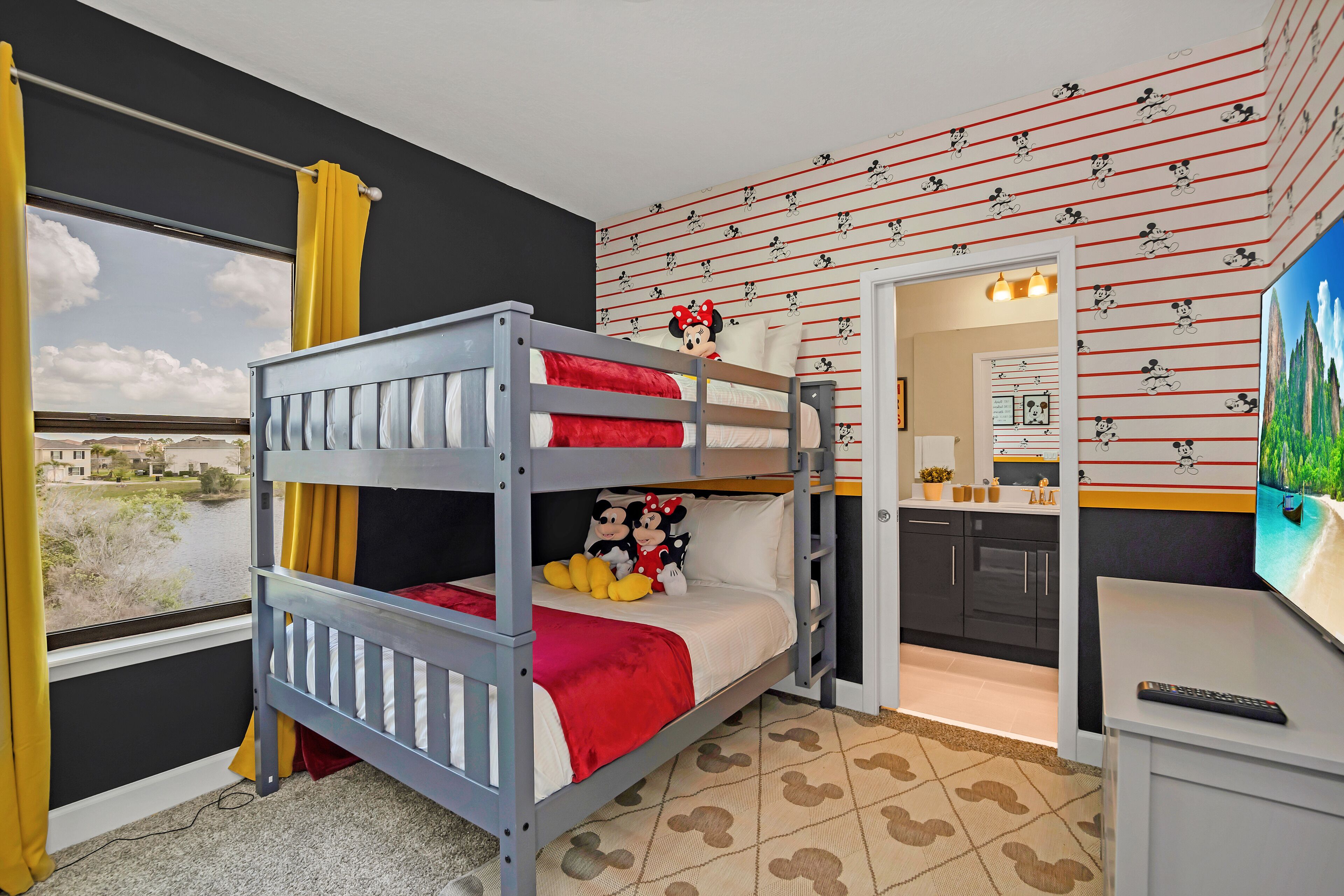 Ein Etagenbett mit Mickey Mouse Kissen und einer Wanddekoration von Mickey Mouse, mit Blick auf einen See.