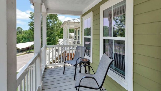 A porch with two chairs, a railing, and a view of a building in the background. - *Cottage #4 @ Fisherman's Landing (boat shelter)* (Langston)