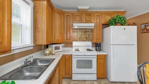 A kitchen with wooden cabinets, a white stove, a white refrigerator, and a microwave. - *Cottage #4 @ Fisherman's Landing (boat shelter)* (Langston)