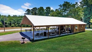 A covered picnic area with tables and benches, surrounded by grass and trees. - *Cottage #4 @ Fisherman's Landing (boat shelter)* (Langston)