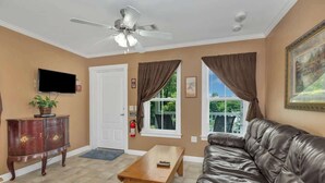 A living room with a leather sofa, a wooden coffee table, a ceiling fan, a television, and a door with windows. - *Cottage #4 @ Fisherman's Landing (boat shelter)* (Langston)