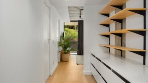 A hallway with a wooden floor, white walls, and a potted plant. Shelves with black and wooden accents line the right side. - Modern 3-Bedroom in the Heart of Bo-Kaap - Netflix (Cape Town)