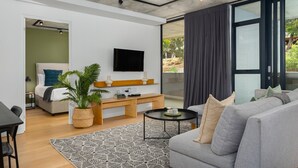 A modern living room with a grey sofa, a black coffee table, a TV mounted on the wall, a wooden bench, and a potted plant. - Modern 3-Bedroom in the Heart of Bo-Kaap - Netflix (Cape Town)