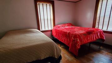 A room with two beds, wooden flooring, and windows with blinds.