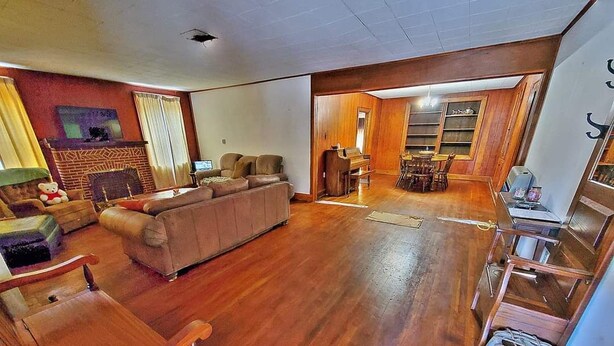 A spacious living room with a large sofa, wooden flooring, a fireplace, and a dining area with a piano. - Cozy & Convenient - 20 Minutes to Charleston WV (Elkview)