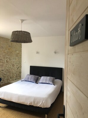 Une chambre avec un mur en pierre, un lit avec une literie blanche et des coussins à motifs, une tête de lit noire, une suspension en fibres tressées et un panneau indiquant « Utah ».