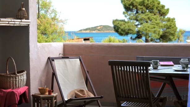 A balcony with a table, chairs, a wicker basket, a hat, and a view of the sea and trees. - Discount (already subtracted) of -40% (Lecci)