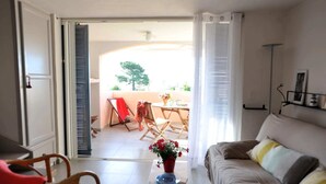 An open living area with a sofa, a dining table with chairs, a small table with a vase of flowers, and a view of the outside balcony. - Discount (already subtracted) of -40% (Lecci)